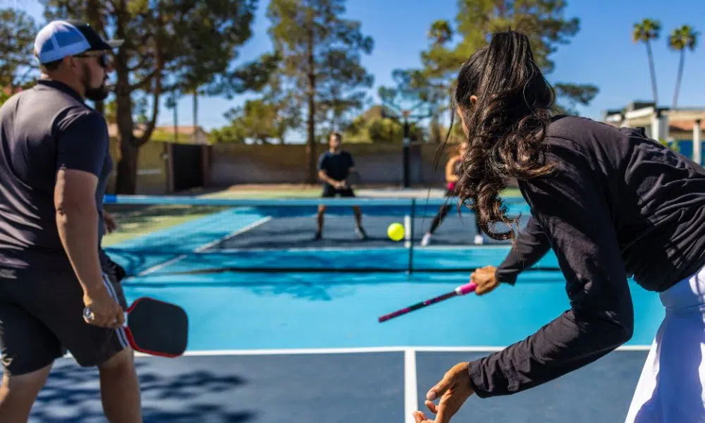 people playing pickleball on a blue court with palm trees in the background